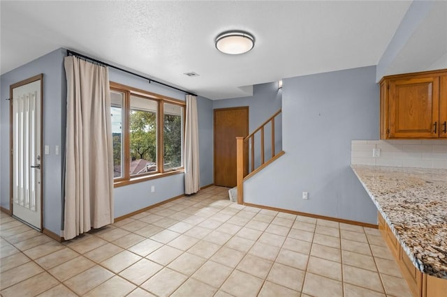 kitchen featuring decorative backsplash, brown cabinetry, baseboards, and visible vents