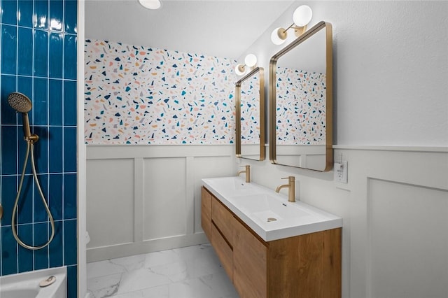 full bathroom with a sink, marble finish floor, wainscoting, and a decorative wall