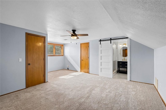 unfurnished bedroom featuring a ceiling fan, vaulted ceiling, a textured ceiling, a barn door, and carpet flooring