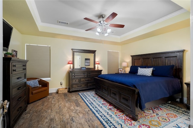 bedroom with wood finished floors, baseboards, visible vents, ornamental molding, and a raised ceiling