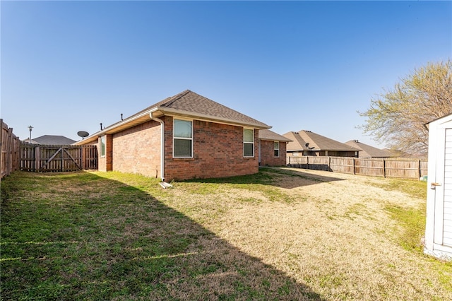 rear view of property featuring a yard, brick siding, a fenced backyard, and a shingled roof