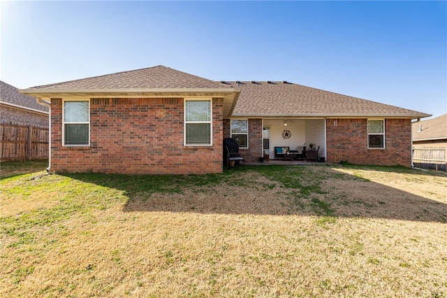 back of house featuring a patio, fence, roof with shingles, a yard, and brick siding