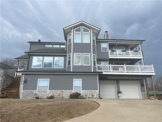 view of front of property with stone siding, stairway, concrete driveway, a garage, and a chimney