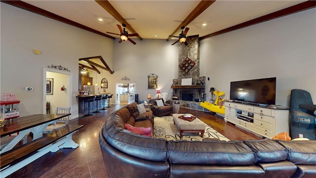 living area with baseboards, beam ceiling, ceiling fan, a stone fireplace, and a towering ceiling