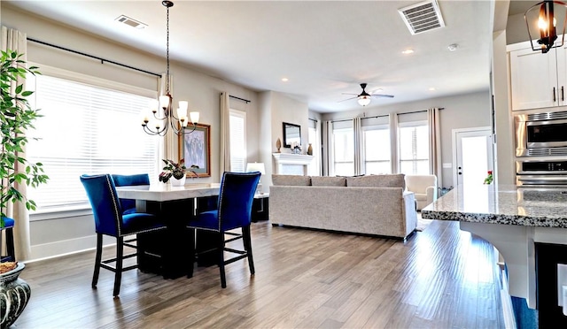 dining space featuring visible vents, baseboards, wood finished floors, and ceiling fan with notable chandelier