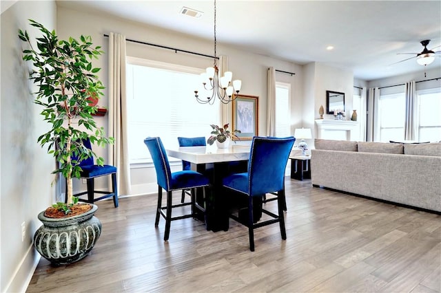 dining area featuring visible vents, ceiling fan with notable chandelier, baseboards, and light wood finished floors