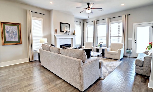 living area featuring a ceiling fan, wood finished floors, visible vents, baseboards, and a fireplace