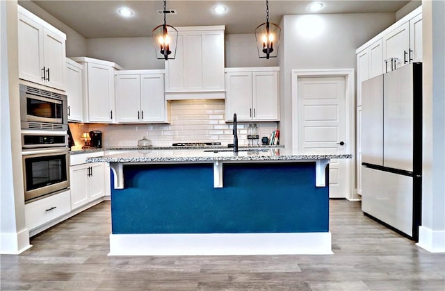 kitchen with stainless steel appliances, light stone counters, an island with sink, a breakfast bar area, and white cabinets