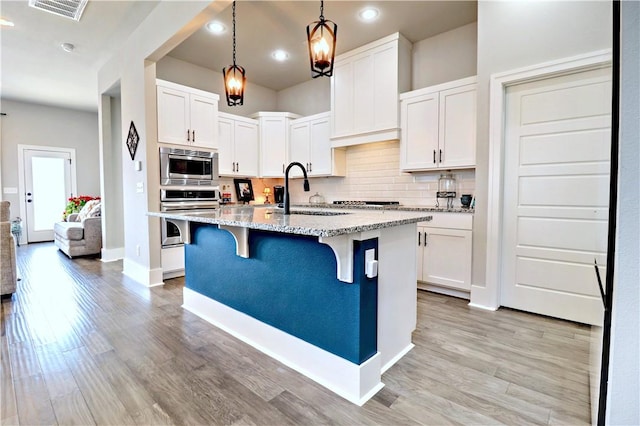 kitchen featuring appliances with stainless steel finishes, a sink, a breakfast bar area, backsplash, and light stone countertops