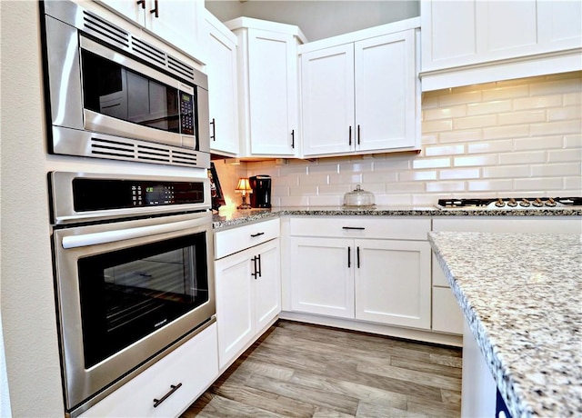 kitchen with light stone counters, light wood-type flooring, white cabinets, appliances with stainless steel finishes, and tasteful backsplash