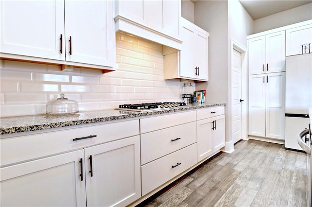 kitchen with light wood finished floors, stainless steel gas cooktop, white cabinets, white refrigerator, and backsplash