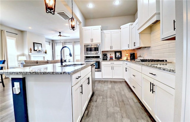 kitchen with ceiling fan, decorative backsplash, appliances with stainless steel finishes, light wood-style floors, and a sink