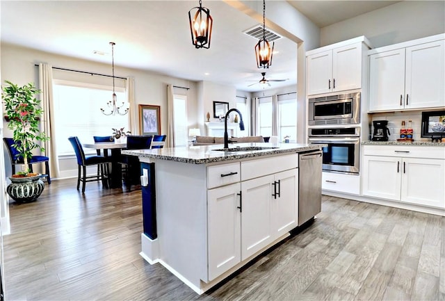 kitchen with visible vents, light wood-type flooring, a sink, light stone counters, and stainless steel appliances