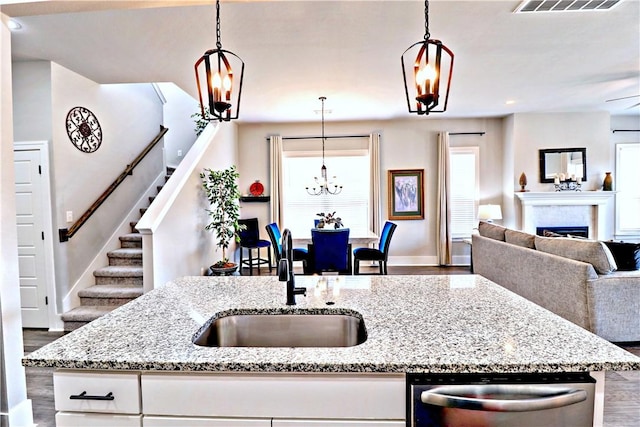 kitchen with light stone counters, wood finished floors, a sink, stainless steel dishwasher, and open floor plan