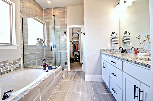 bathroom with vanity, baseboards, a shower stall, a spacious closet, and a garden tub