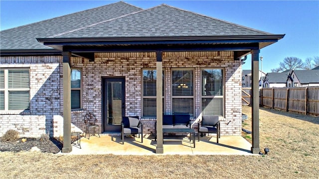 back of property with roof with shingles, fence, brick siding, and a patio area