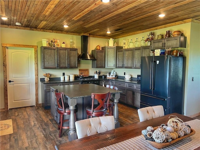 kitchen featuring dark countertops, wooden ceiling, freestanding refrigerator, dark wood-style floors, and wall chimney exhaust hood