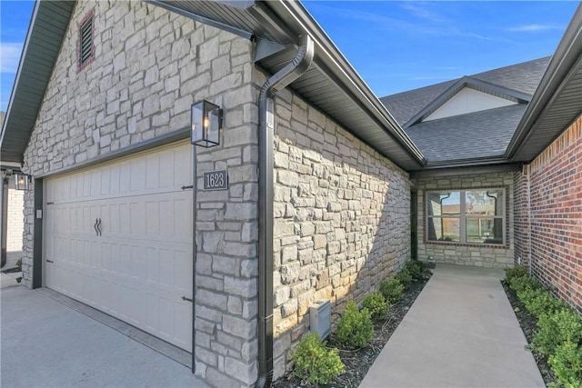 view of home's exterior with stone siding, an attached garage, a shingled roof, and driveway