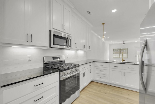 kitchen with light wood-type flooring, dark countertops, white cabinetry, stainless steel appliances, and a peninsula