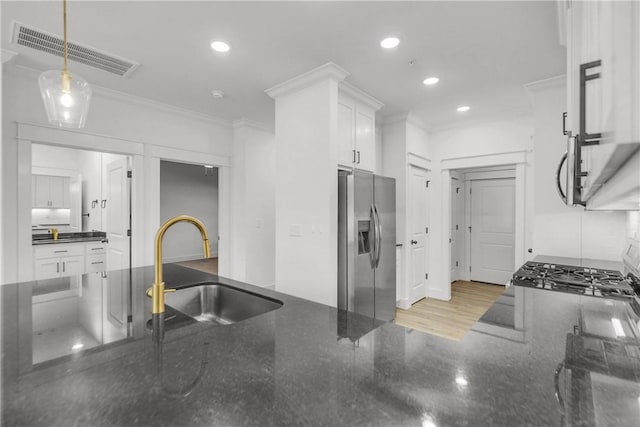 kitchen with visible vents, a sink, white cabinetry, stainless steel fridge, and crown molding