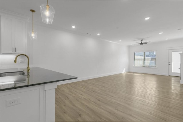 kitchen with light wood-style flooring, ceiling fan, a sink, white cabinets, and dark countertops