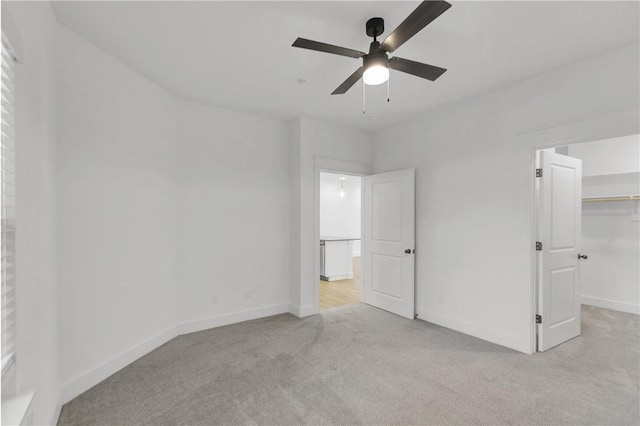 unfurnished bedroom featuring carpet, baseboards, ceiling fan, a closet, and a walk in closet