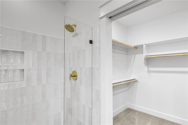 bathroom with tiled shower, a walk in closet, and baseboards