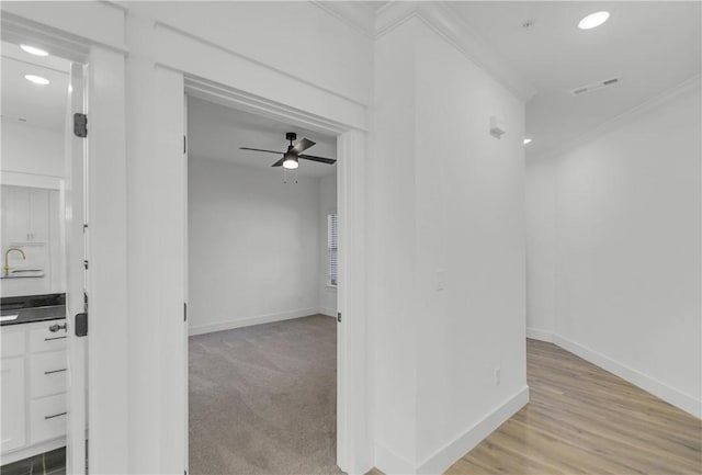 corridor with light wood finished floors, baseboards, light colored carpet, ornamental molding, and recessed lighting