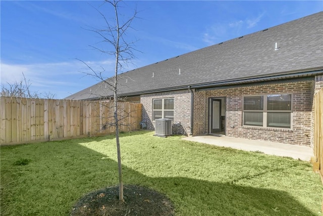 rear view of house featuring a lawn, central AC, fence, a shingled roof, and brick siding