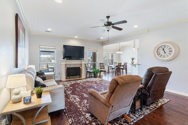 living room with crown molding, baseboards, a tile fireplace, a ceiling fan, and dark wood-style flooring