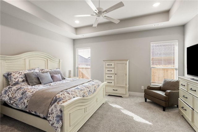 bedroom with a tray ceiling, light colored carpet, recessed lighting, and baseboards