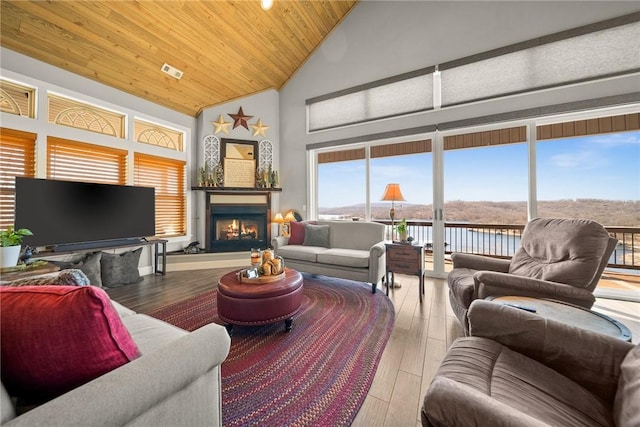 living area featuring visible vents, high vaulted ceiling, wood finished floors, a lit fireplace, and wood ceiling