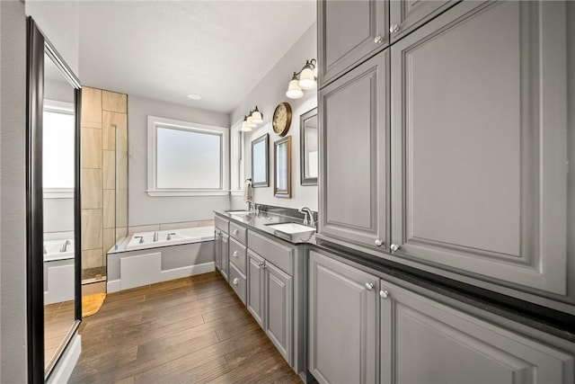 full bathroom featuring a garden tub, wood finished floors, double vanity, and a sink