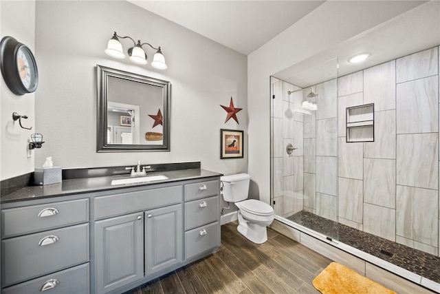 full bathroom featuring baseboards, toilet, tiled shower, wood finished floors, and vanity