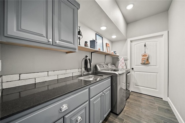 laundry area featuring washing machine and clothes dryer, baseboards, dark wood finished floors, cabinet space, and a sink