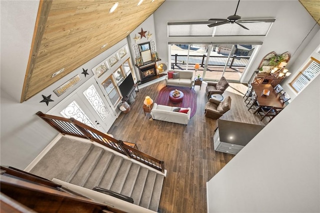 living area with ceiling fan, a high ceiling, a lit fireplace, and wood finished floors