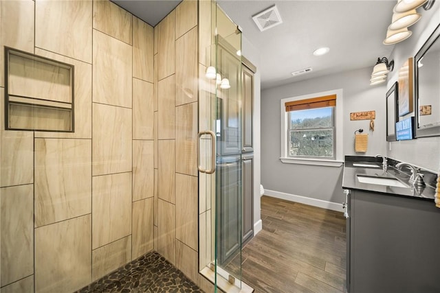 full bath featuring visible vents, a shower stall, baseboards, wood finished floors, and a sink