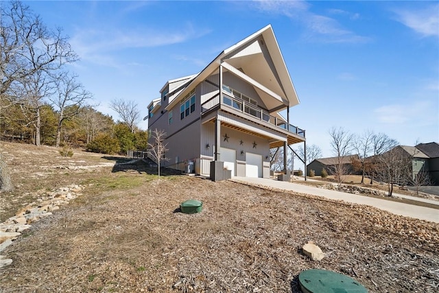 view of property exterior with a balcony, an attached garage, driveway, and central AC