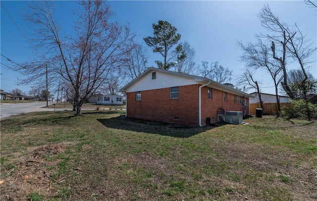 view of side of property with driveway, central AC, crawl space, a lawn, and brick siding