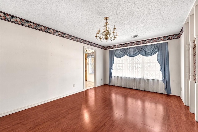 spare room featuring visible vents, a textured ceiling, wood finished floors, baseboards, and a chandelier