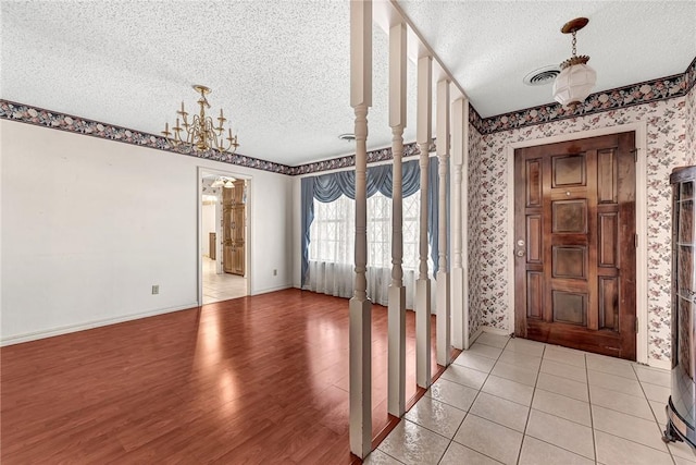 foyer entrance featuring visible vents, wallpapered walls, an inviting chandelier, light wood-style flooring, and a textured ceiling