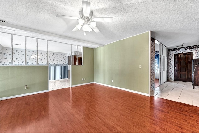 empty room with wood finished floors, visible vents, baseboards, ceiling fan, and a textured ceiling