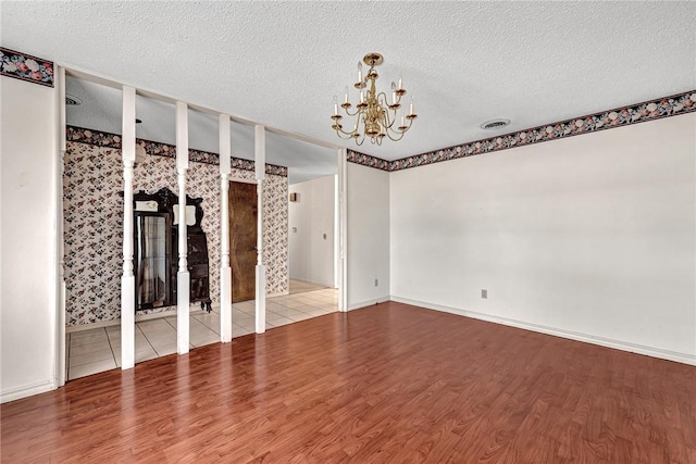 empty room featuring visible vents, a textured ceiling, wood finished floors, baseboards, and a chandelier