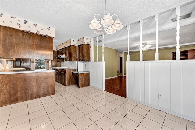 kitchen featuring ceiling fan with notable chandelier, under cabinet range hood, a textured ceiling, a peninsula, and light tile patterned floors