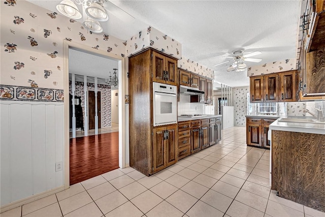 kitchen featuring wallpapered walls, white oven, light tile patterned flooring, and under cabinet range hood