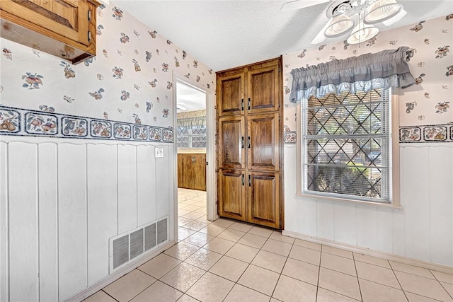 interior space featuring light tile patterned floors, brown cabinetry, visible vents, wallpapered walls, and a textured ceiling