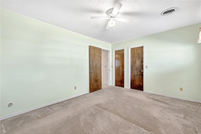 carpeted empty room featuring baseboards, visible vents, a textured ceiling, and ceiling fan