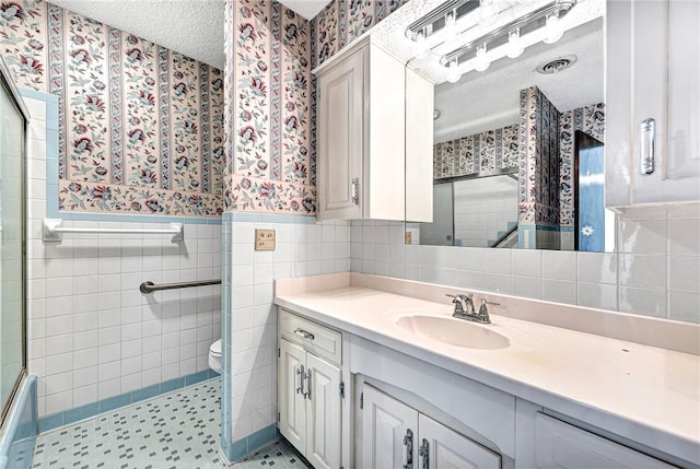 bathroom with wainscoting, a textured ceiling, wallpapered walls, and vanity