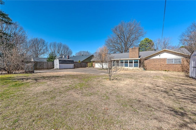 view of yard with fence, driveway, an outdoor structure, a garage, and a storage shed