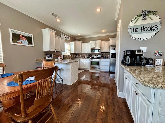 kitchen featuring visible vents, dark wood-type flooring, ornamental molding, appliances with stainless steel finishes, and a peninsula